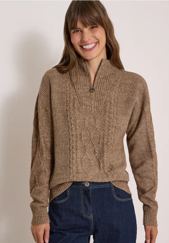 Femme souriante en pull marron à torsades, col montant zippé, style décontracté.
