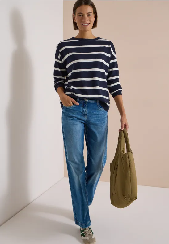 Frau trägt blau-weiß gestreiften Pullover, lockere Jeans und hält olivefarbene Tasche.