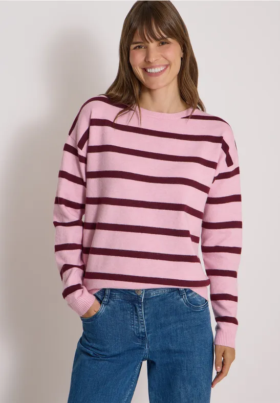 Femme souriante en pull rayé rose et jean bleu.