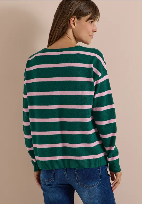 Femme de dos portant un pull rayé vert, blanc et rose et un jean bleu sur fond neutre.