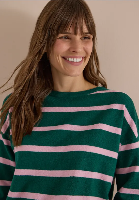Femme souriante portant un pull à rayures vertes et roses.