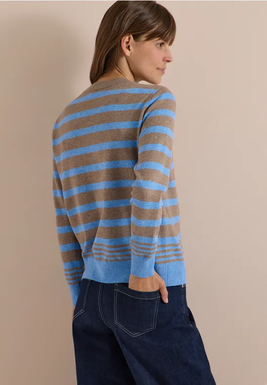 Une femme de profil porte un pull rayé beige et bleu clair assorti à un jean bleu foncé.
