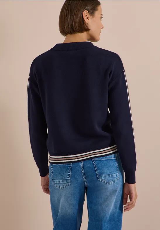 Rückenansicht einer Frau in marineblauem Pullover mit gestreiftem Saum und blauen Jeans.