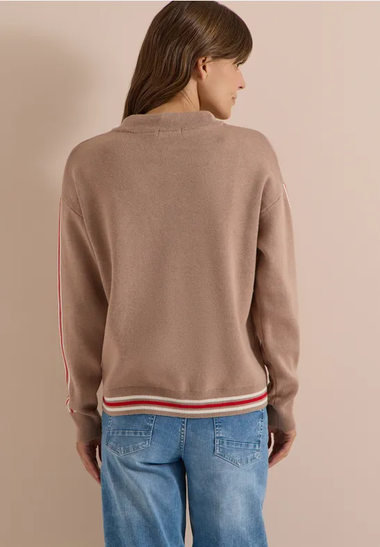 Frau von hinten mit taupefarbenem Strickpullover, rot-weiß gestreiftem Bund und blauen Jeans.