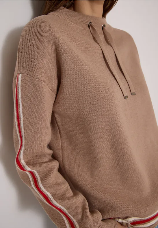 Beiger Pullover mit Kapuze und kontrastierenden roten und weißen Streifen an den Ärmeln.