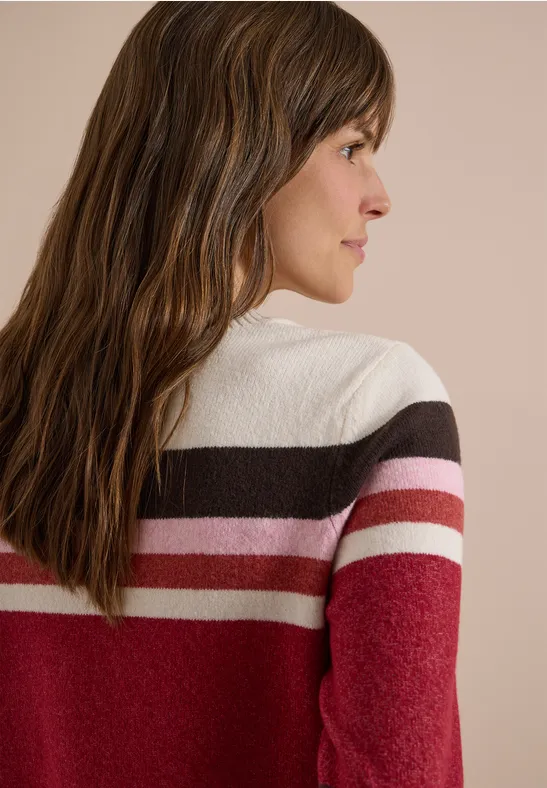 Vue de profil d’une femme aux longs cheveux bruns portant un pull rayé rouge, rose, blanc et marron.