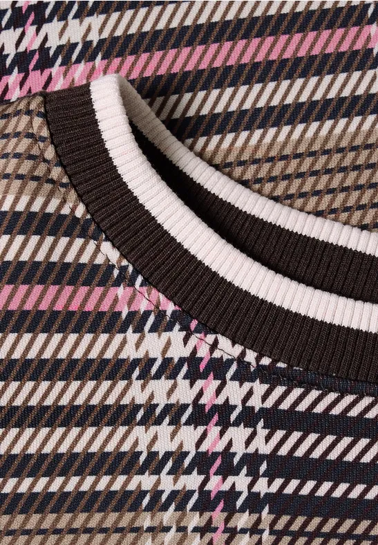 Nahaufnahme eines karierten Strickpullovers mit Hahnentrittmuster und kontrastfarbenem Rundhalsausschnitt.