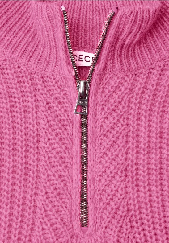 Nahaufnahme eines rosa Strickpullovers mit Zopfmuster und silbernem Reißverschluss.
