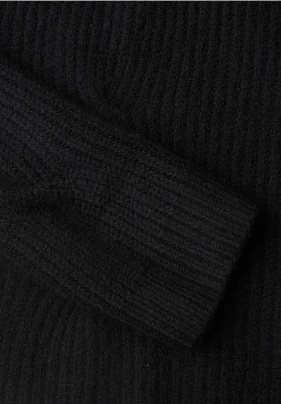 Schwarzer, grob gerippter Strickpullover mit sichtbar gefaltetem Ärmel auf hellem Untergrund.
