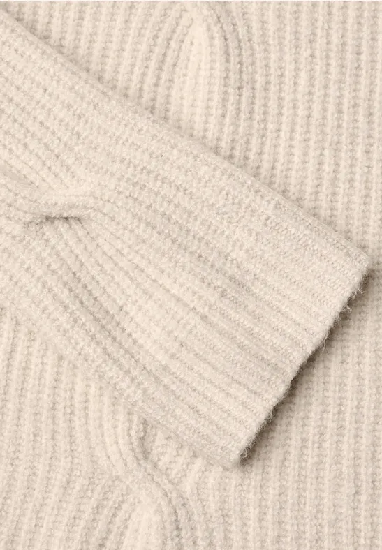 Close-up van een beige gebreide trui met gevlochten patroon.