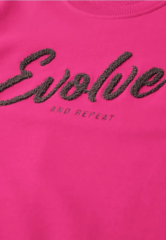 Pinkes T-Shirt mit schwarzem Schriftzug 'Evolve' und kleinem 'and repeat'.