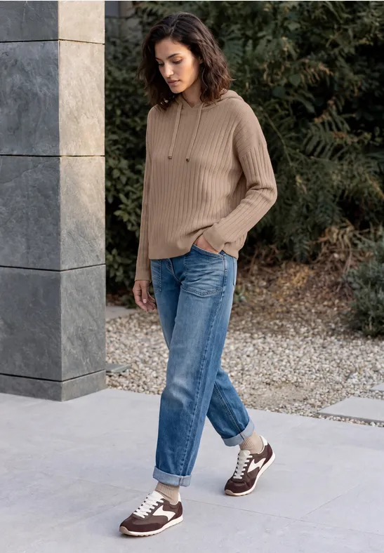 Femme en pull beige en maille et jean, baskets marron et blanches, marche dans le jardin.