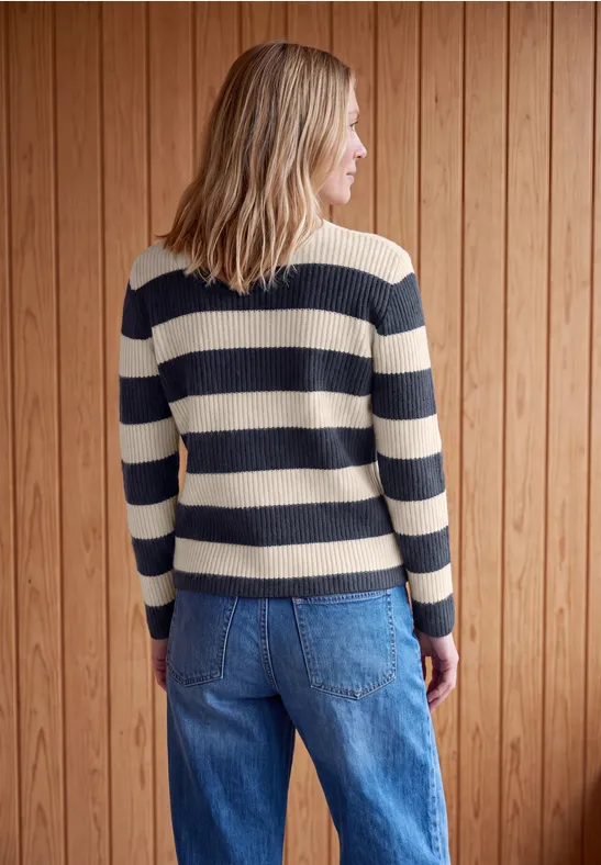 Femme de dos portant un pull rayé bleu et beige et un jean, devant un mur en bois.