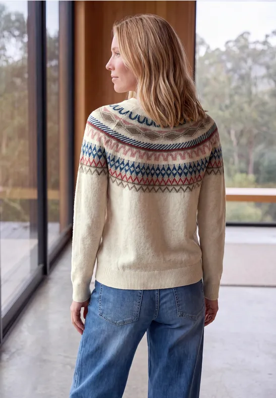 Kobieta stoi tyłem, ma na sobie jasny sweter Fair Isle i dżinsy, przed dużymi oknami w jasnym wnętrzu.
