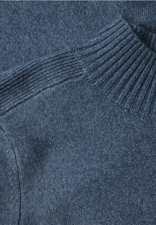 Gros plan d'un pull en maille bleu foncé à col roulé et texture raffinée.