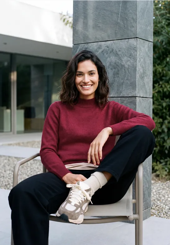 Une femme souriante est assise confortablement sur une chaise devant un bâtiment moderne.