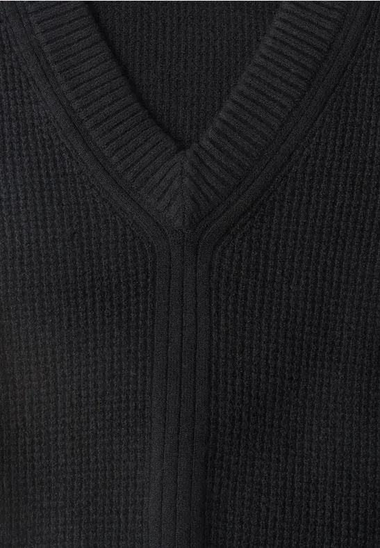 Nahaufnahme eines schwarzen, V-förmigen Strickpullovers mit sichtbarer Struktur.