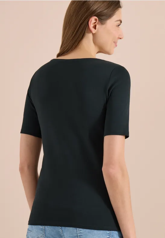 Rückenansicht einer Frau mit schwarzem kurzärmligem Oberteil und blauer Jeans vor hellem Hintergrund.