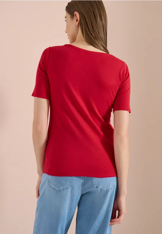 Vrouw van achteren in een rood T-shirt en lichtblauwe spijkerbroek voor een neutrale achtergrond.