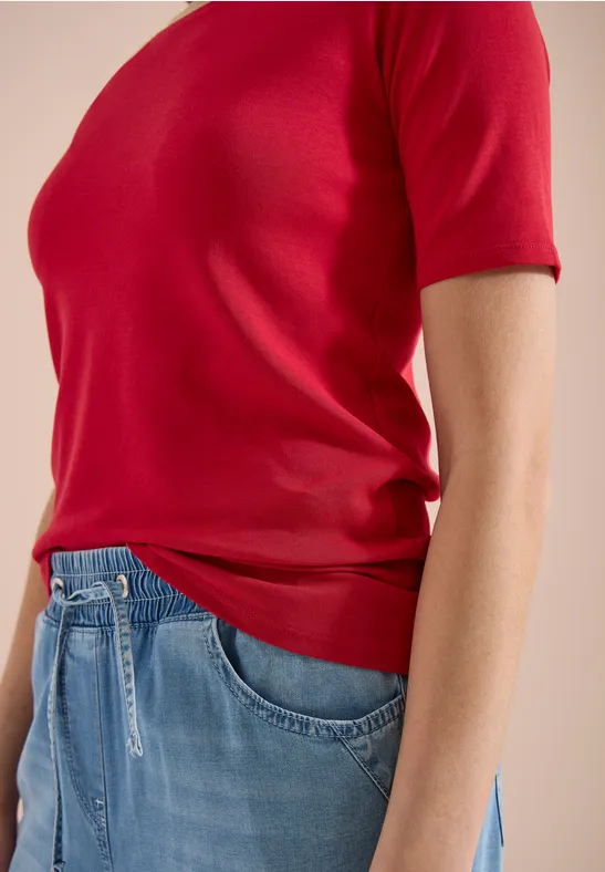 Bovenlichaam van een persoon in een rood T-shirt met korte mouwen en een blauwe jeans