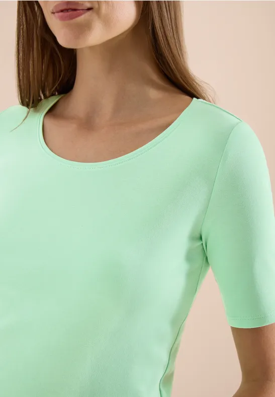 Oberkörper einer Frau in mintgrünem, kurzärmeligem Shirt mit rundem Ausschnitt.