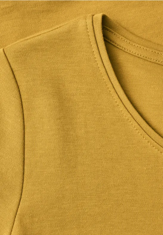 Nahaufnahme eines ockerfarbenen T-Shirt-Ausschnitts und -Ärmels.