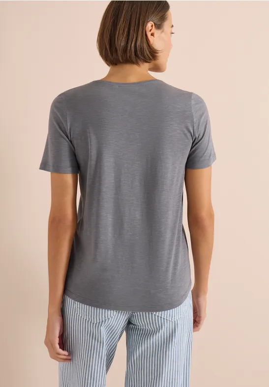 Persoon van achteren in grijs t-shirt en lichtblauwe gestreepte broek tegen beige achtergrond.