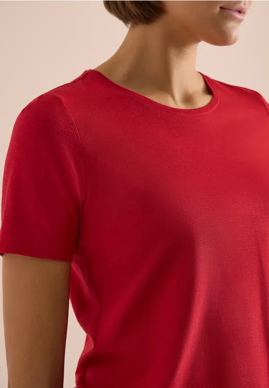 Nahaufnahme eines weiblichen Oberkörpers in rotem, kurzärmeligen T-Shirt.