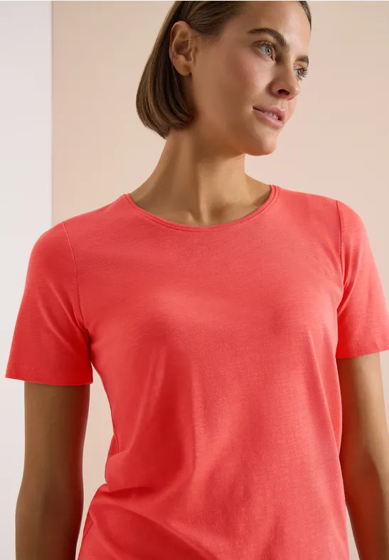 Person trägt rotes T-Shirt vor hellem Hintergrund.