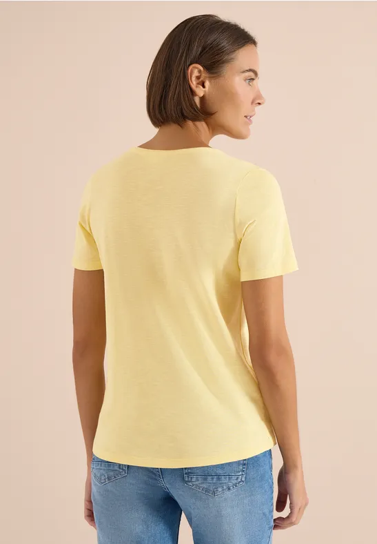 Een persoon gezien van achteren draagt een geel T-shirt en een blauwe spijkerbroek.