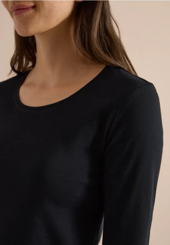 Eine Frau trägt ein schlichtes schwarzes Langarmshirt mit rundem Ausschnitt.