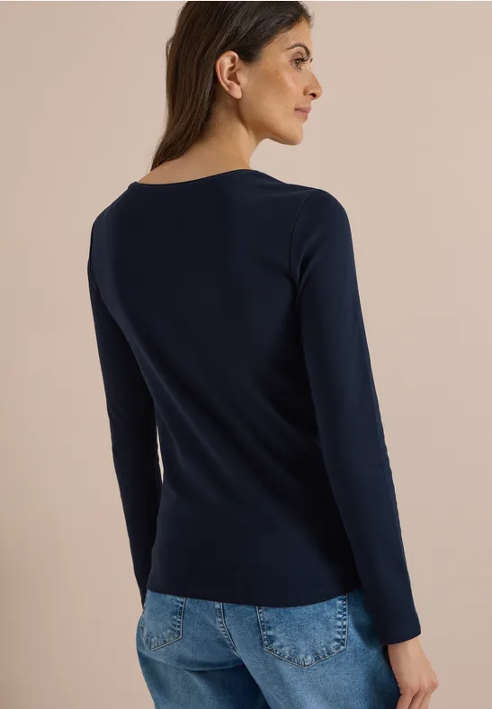 Frau von hinten in dunkelblauem Langarmshirt und heller Jeans.