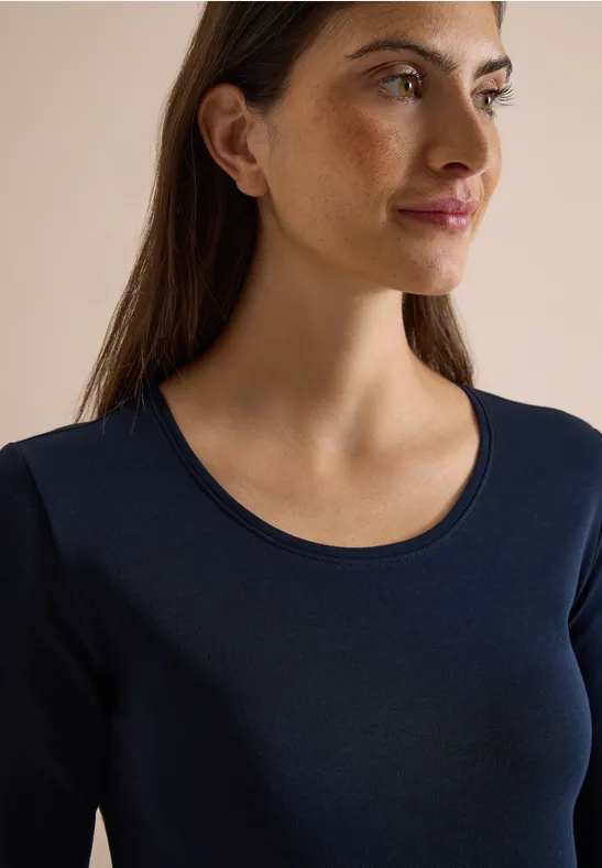 Eine junge Frau mit braunen Haaren trägt ein dunkelblaues Langarmshirt und blickt seitlich.