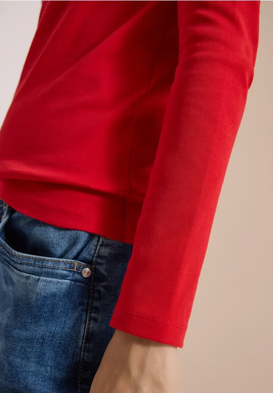 Nahaufnahme einer Person in rotem Langarmshirt und blauen Jeans, Fokus auf Arm und Taille