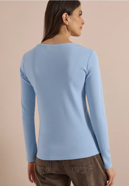 Frau von hinten in schlichtem hellblauen, langärmligen Shirt vor neutralem Hintergrund.