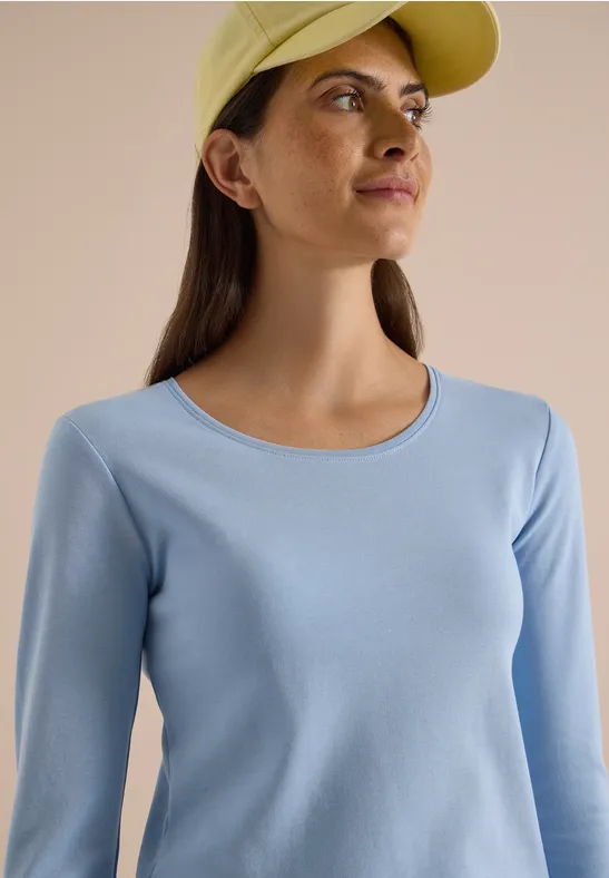 Frau mit gelber Cap und hellblauem Langarmshirt blickt seitlich, Sommersprossen auf dem Gesicht.