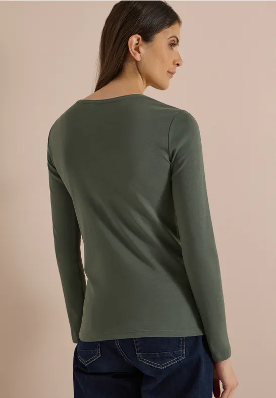 Frau in grünem Langarmshirt, von hinten im seitlichen Profil vor neutralem Hintergrund.