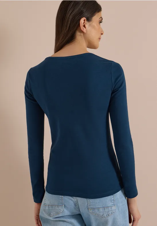 Frau von hinten in Navy-Blau Langarmshirt und Jeans vor neutralem Hintergrund.