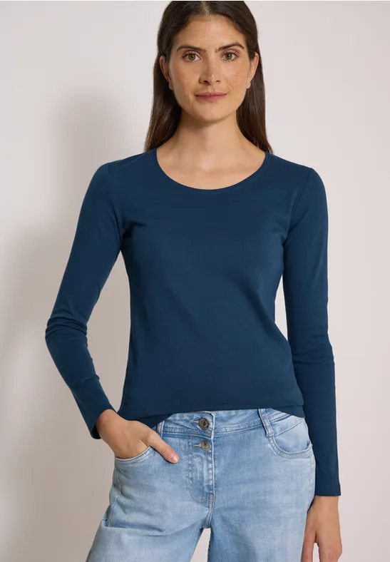 Frau mit dunkelblauem Langarmshirt und Jeans, Hand in Tasche, frontal stehend