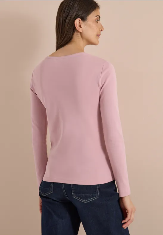 Frau von hinten in rosafarbenem Langarmshirt und blauen Jeans vor hellem Hintergrund
