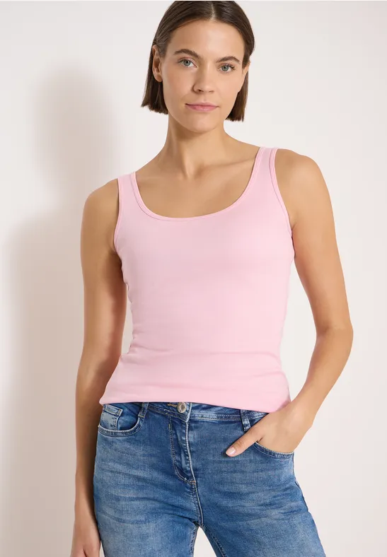 Femme portant un haut sans manches rose et un jean bleu sur fond neutre.