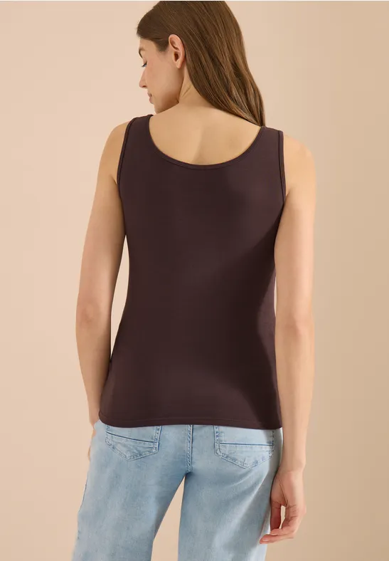 Femme vue de dos portant un débardeur marron et un jean bleu clair devant un mur beige