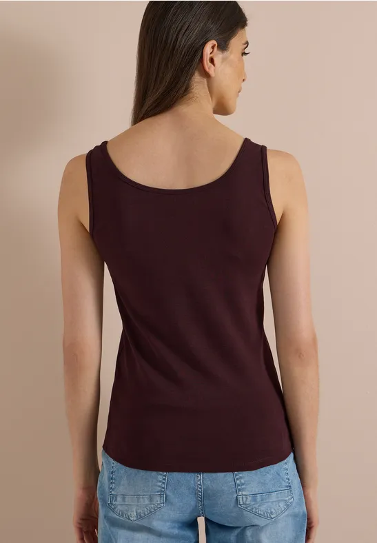 Een vrouw van achteren met een bordeauxrode mouwloze top en blauwe jeans.
