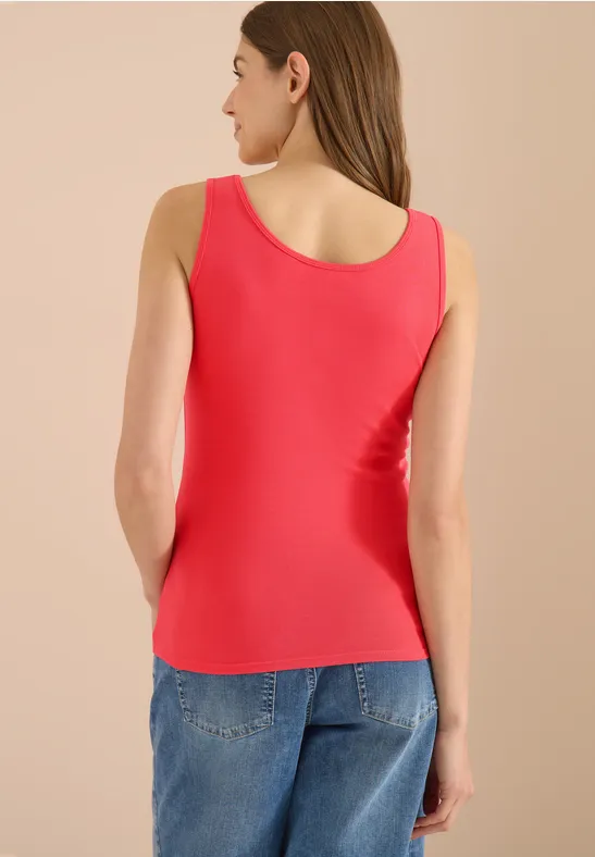 Femme de dos portant un débardeur rouge et un jean bleu sur fond clair.