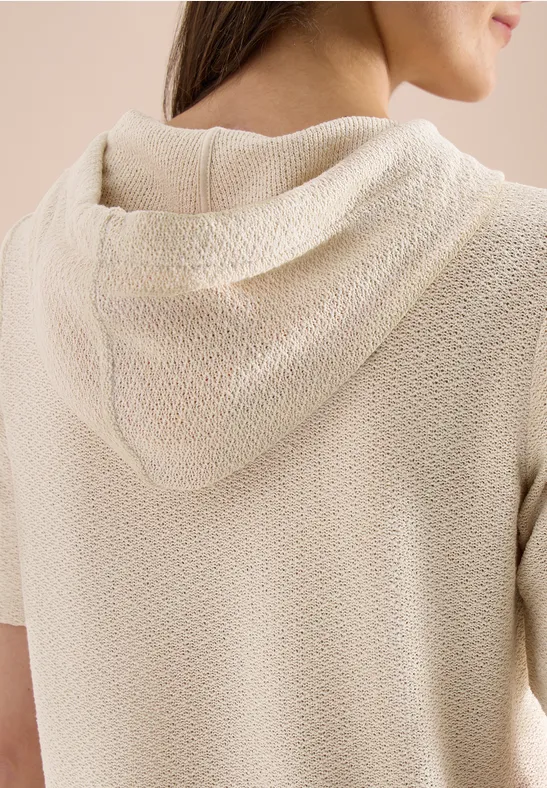 Achteraanzicht van een vrouw in een beige, gestructureerde korte mouwen hoodie.