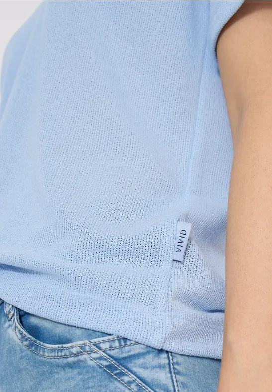 Zijaanzicht van persoon in lichtblauw shirt en blauwe jeans, klein merkje zichtbaar.