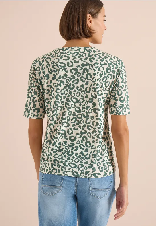 Vrouw van achteren in een kort groen shirt met luipaardprint en lichtblauwe jeans.
