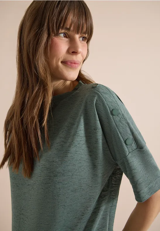 Vrouw opzij met groen shirt met halflange mouwen en knopen op de schouder voor beige achtergrond