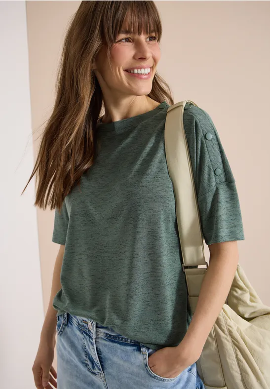 Vrouw in groen T-shirt met korte mouwen en knopen, blauwe jeans en rugzak over de schouder