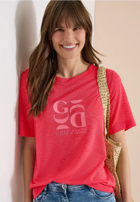 Frau trägt rotes T-Shirt mit Aufdruck und Korbtasche über der Schulter